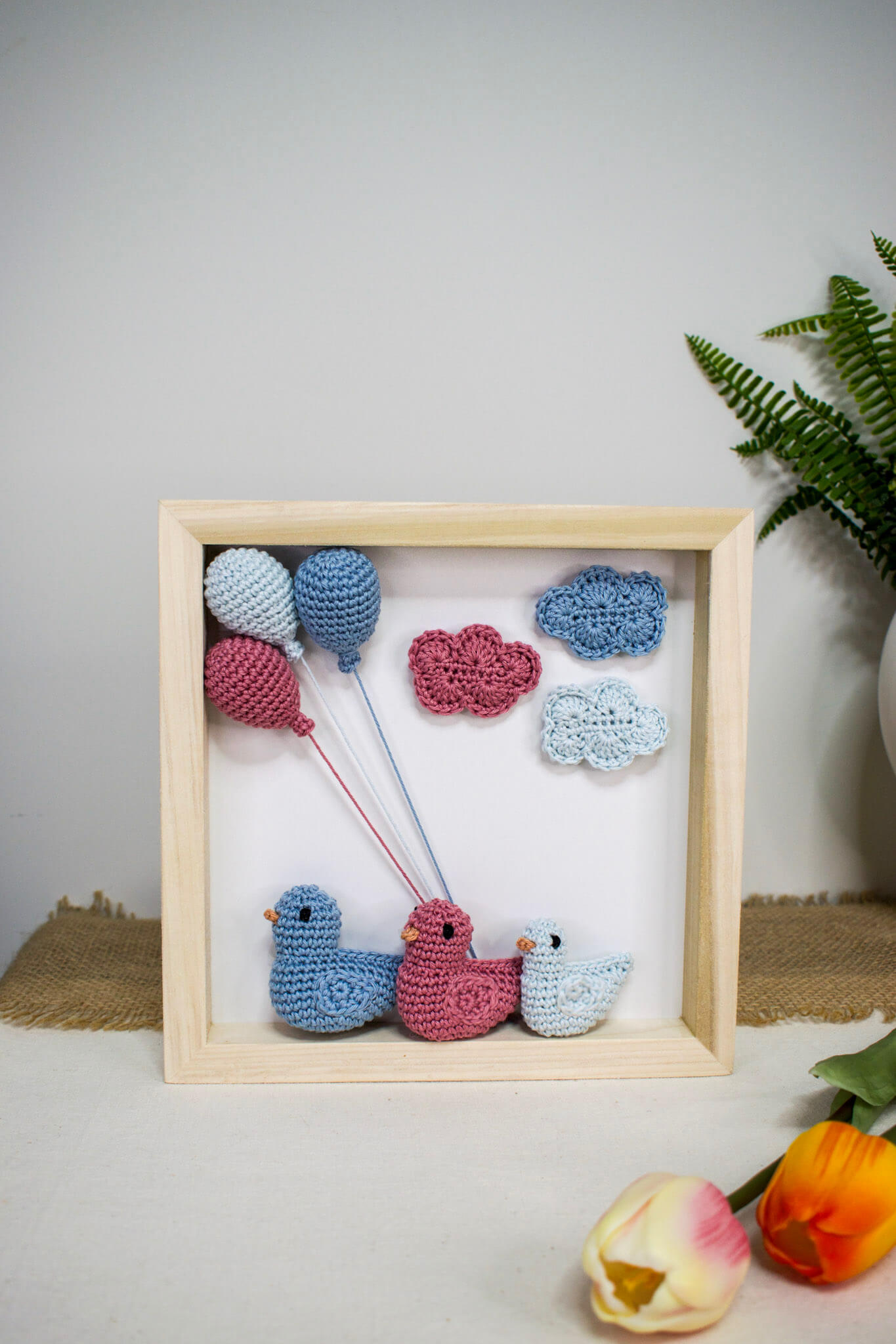 Χειροποίητο ξύλινο κάδρο με πλεκτά amigurumi παπάκια που αναπαριστούν μια οικογένεια με αγοράκι, διακοσμημένο με γαλάζια και ροζ πλεκτά μπαλόνια και σύννεφα.