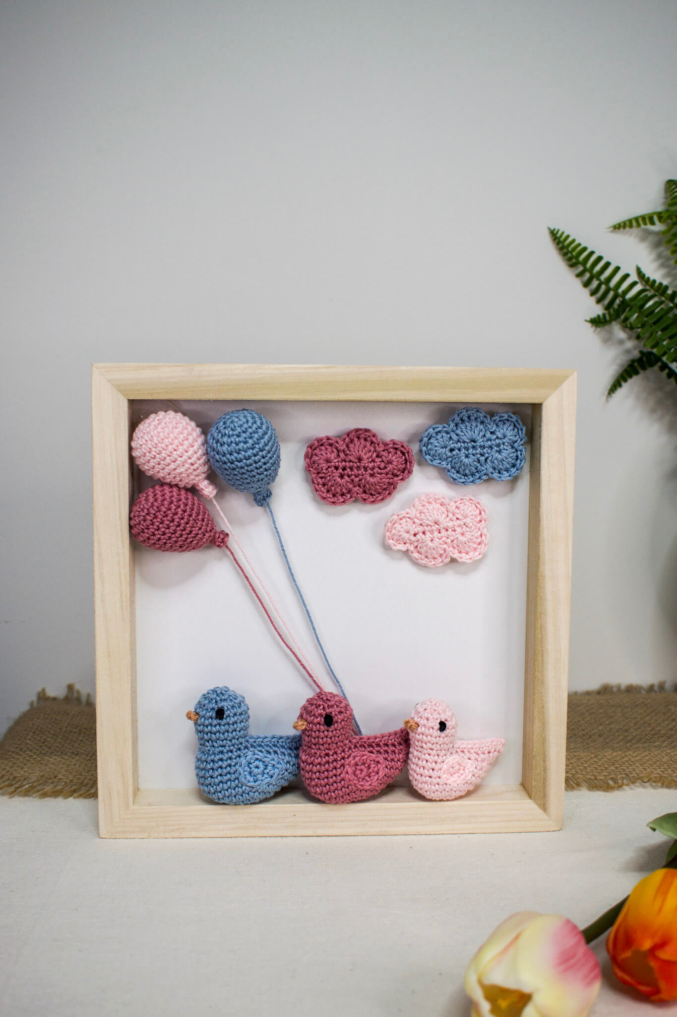 Χειροποίητο ξύλινο κάδρο με πλεκτά amigurumi παπάκια που αναπαριστούν μια οικογένεια με κοριτσάκι, διακοσμημένο με ροζ και γαλάζια πλεκτά συννεφάκια και μπαλόνια.
