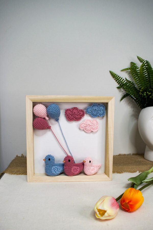 Χειροποίητο ξύλινο κάδρο με πλεκτά amigurumi παπάκια που αναπαριστούν μια οικογένεια με κοριτσάκι, διακοσμημένο με ροζ και γαλάζια πλεκτά συννεφάκια και μπαλόνια.
